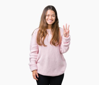 Gösterilen ve parmakları ile işaret izole arka plan üzerinde pembe kış kazak giyen genç güzel esmer kadın kendinden emin ve mutlu gülümseyerek iken üçüncü.