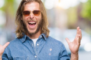 Genç yakışıklı adam uzun saçlı deli ve çığlık kaldırdı ve kapalı gözleri heyecanlı silah ile başarı için deli kutluyor izole arka plan üzerinde güneş gözlüğü takıyor. Kazanan kavramı