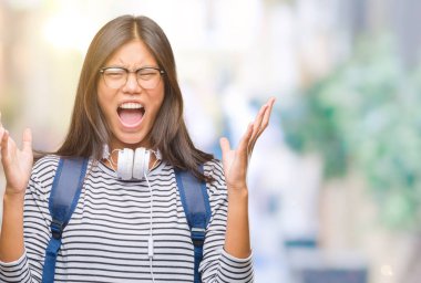 Genç Asyalı öğrenci kadın giyen kulaklık ve sırt çantası kızgın ve silah ile başarı için deli kutluyor izole arka plan üzerinde kaldırdı ve heyecanlı çığlık gözler kapalı. Kazanan kavramı