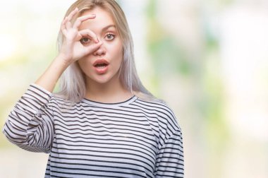 Sürpriz yüz, göz parmaklarının arasından seyir ile ok jest yapıyor izole arka plan üzerinde sarışın genç kadın şok. İmansız ifade.