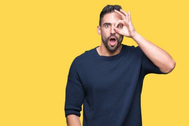 Sürpriz yüz, göz parmaklarının arasından seyir ile ok jest yapıyor izole arka plan üzerinde kazak giyen genç yakışıklı adam şok. İmansız ifade.