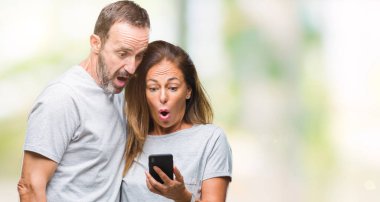 Orta yaş İspanyol çift mesaj mesaj smartphone ver üzerinde arka plan bir sürpriz yüz, korkuyor ve heyecanlı korku ifadesi ile şok korkmuş izole