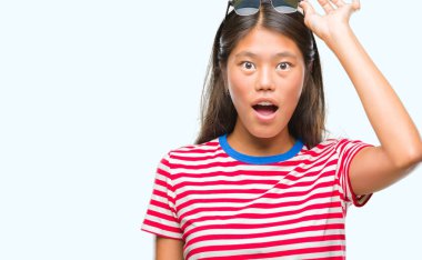 Genç Asyalı kadın korkuyor ve şok sürpriz ifade, korku ve heyecan yüz ile izole arka plan üzerinde güneş gözlüğü takıyor.