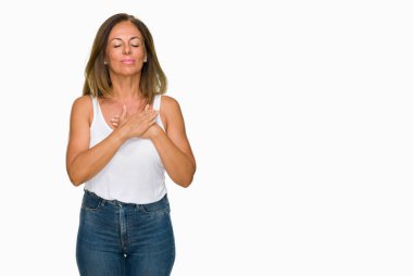 Eller üzerinde izole arka plan ile gülümseyen güzel orta yaş rahat yetişkin kadın göğüs kapalı gözler ve yüzünde minnettar jest ile. Sağlık kavramı.