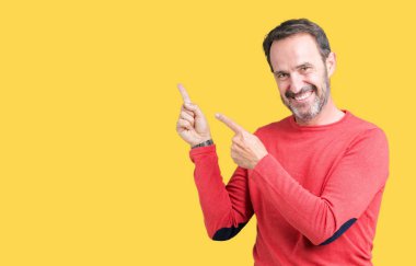 Gülümseyen ve iki ile işaret kamera bakarak izole arka plan üzerinde kış kazak giymiş yakışıklı orta yaş ağarmış komuta sizde eller ve yan parmak.