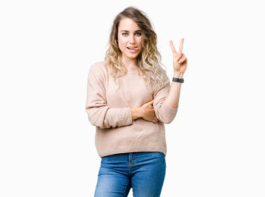 Mutlu yüz zafer işareti yaparken kameraya göz kırpıyor ile gülümseyen izole arka plan üzerinde sweatershirt giyen güzel genç sarışın kadın. İki numaralı.