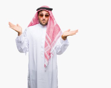 Keffiyeh izole arka plan clueless ve şaşkın bir ifadeyle kollar ve eller kaldırdı üzerinde giyen genç yakışıklı adam. Şüphe kavramı.