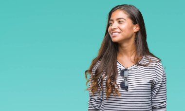 Genç güzel Arap kadın uzak tarafına yüzünde, doğal ifade gülümseme ile seyir izole arka plan üzerinde güneş gözlüğü takıyor. Kendine güvenen gülüyor.