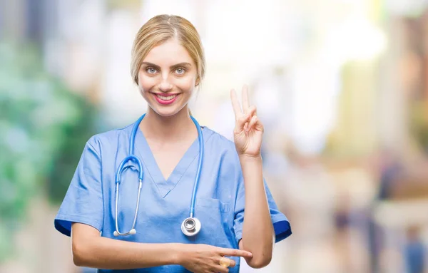 年轻美丽的金发医生护士护士妇女在孤立的背景微笑着与幸福的脸眨眼对着相机做胜利的标志 — 图库照片