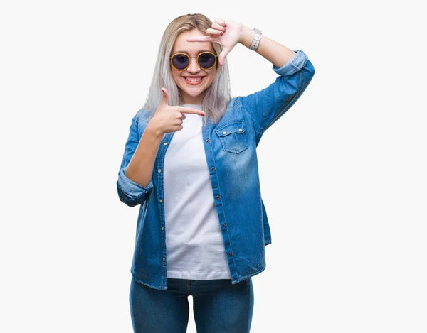 若いブロンドの女性は 笑顔と幸せそうな顔で指手作りフレーム分離の背景の上にサングラスをかけています 創造性と写真のコンセプト — ストック写真