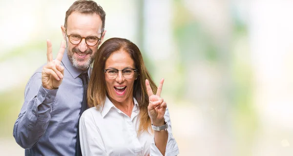 中年愛眼鏡をかけて勝利のサインを行うカメラでウィンクしている幸せそうな顔を浮かべて孤立の背景の上でヒスパニック系のカップル — ストック写真