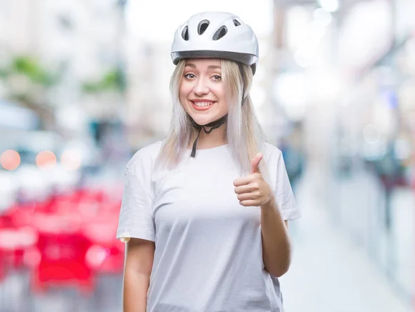 年轻的金发女子穿着自行车安全头盔在孤立的背景做愉快的拇指手势与手 批准表达式看着相机显示成功 — 图库照片