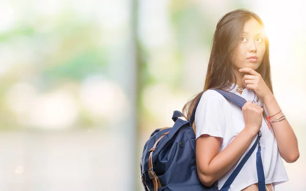 Young asian woman wearing backpack and headphones over isolated background serious face thinking about question, very confused idea