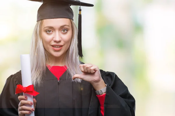自分自身に驚き顔人差し指と孤立の背景上の学位を保持する大学院の制服を着て若いブロンドの女性 — ストック写真