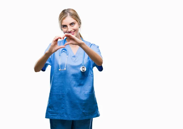 若い美しい金髪の医者の外科医看護師女性恋ハートマークと手で形を示す笑みを浮かべて孤立の背景の上 ロマンチックな概念 — ストック写真