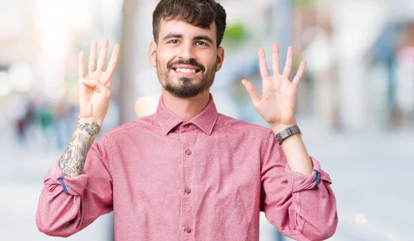 Yakışıklı delikanlı gösterilen ve parmakları ile işaret izole arka plan üzerinde pembe gömlek giymiş numara 9 kendinden emin ve mutlu gülümseyerek süre.