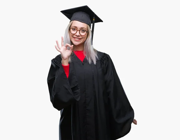 若いブロンドの女性は 孤立した背景を浮かべて手と指で サインをしている肯定的な上の大学院の制服を着ています 成功した式 — ストック写真