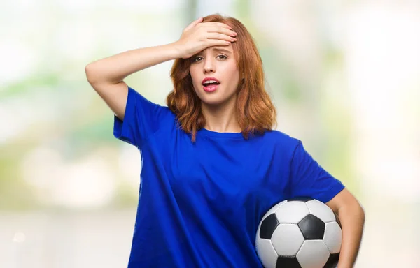 若くてきれいな女性の頭の上の手を強調したサッカー サッカー ボールを保持している孤立した背景の上に恥と驚きの顔で衝撃を与えた怒っているとイライラします 恐怖と動揺の間違い — ストック写真