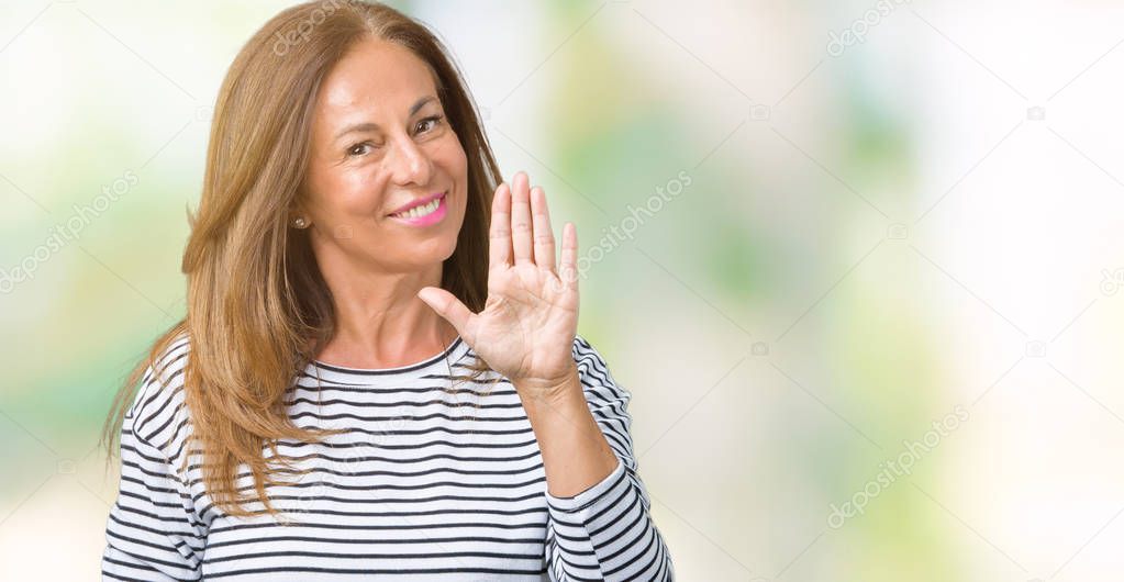 Beautiful middle age woman wearing stripes sweater over isolated background Waiving saying hello happy and smiling, friendly welcome gesture