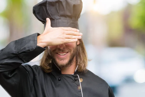 Young handsome cook man with long hair over isolated background smiling and laughing with hand on face covering eyes for surprise. Blind concept.