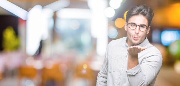 Young handsome man wearing glasses over isolated background looking at the camera blowing a kiss with hand on air being lovely and sexy. Love expression.