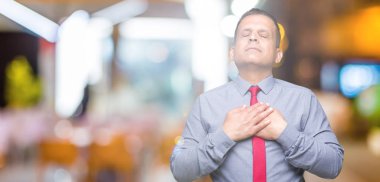 Orta yaş Arap kapalı gözler ile göğüs ellerinde ve yüzünde minnettar jest ile gülümseyen izole arka plan üzerinde kırmızı kravat giyen adam. Sağlık kavramı.