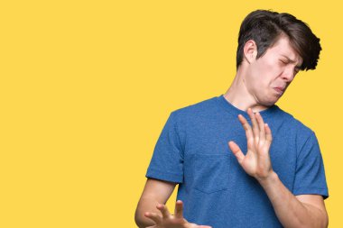 İzole arka plan üzerinde mavi t-shirt giyen genç yakışıklı adam tiksinti ifadesi, memnun ve korkulu tiksinti yüz yapıyorsun çünkü nefret tepki. Elleriyle kaldırdı. Sinir bozucu kavramı.