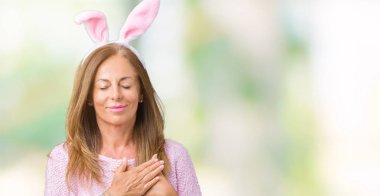 Paskalya tavşan kulakları ile gülümseyen izole arka plan üzerinde giyen orta yaş esmer kadın kapalı gözler ve yüzünde minnettar jest ile göğüs üzerinde eller. Sağlık kavramı.