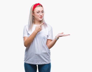 Hayret ve el ile sunulması ve parmak ile işaret ederken kameraya gülümseyen izole arka plan üzerinde gözlüklü sarışın genç kadın.