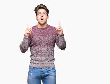 Yakışıklı delikanlı hayrete ve yukarıya bakıyor ve parmakları ile işaret ve silah kaldırdı sürpriz izole arka plan üzerinde gözlük.