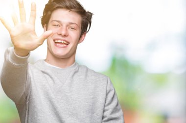 Gösterilen arka plan üzerinde sweatshirt giyen genç yakışıklı sportif adam izole ve parmakları ile işaret kendinden emin ve mutlu gülümseyerek süre beş numara.