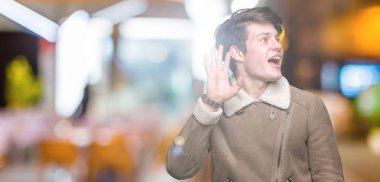 Üzerinde kış ceket giyen genç yakışıklı adam arka plan bir işitme söylenti ya da dedikodu için dinleme kulak üzerinde el ile gülümseyen izole. Sağırlık kavramı.