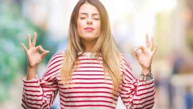 Genç güzel kadın rahat çizgili kış kazak izole arka plan üzerinde dinlenmek ve gülümseyen gözlerle kapalı parmak jestle meditasyon yapıyor. Yoga kavramı.