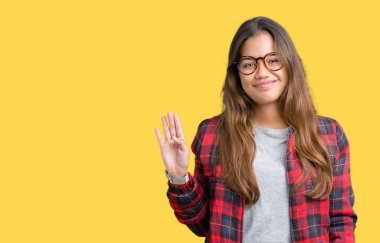 Ceket ve izole arka plan Waiving mutlu selam söyleyerek üzerinde gözlük ve gülümseyen, dostça karşılama jest giyen genç güzel esmer kadın