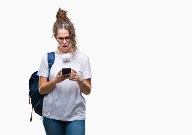 Sırt çantası, kulaklık ve smartphone izole arka şok sürpriz yüzü, korkuyor ve korku ifadesi ile heyecanlı olan korkmuş üzerinde giyen genç esmer öğrenci kız