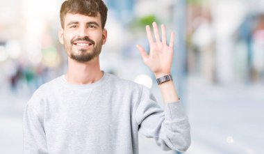 Gösterilen arka plan üzerinde sweatshirt giyen genç yakışıklı adam izole ve parmakları ile işaret kendinden emin ve mutlu gülümseyerek süre beş numara.