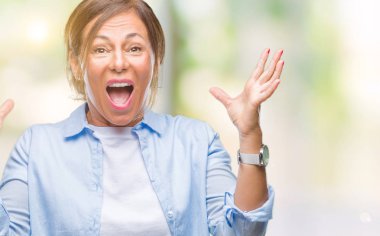 Orta yaş üst düzey İspanyol kadın deli kutluyor arka plan izole ve başarı için kaldırdı kollarını açarak hayrete ve heyecanlı çığlık gözleri açık. Kazanan kavramı