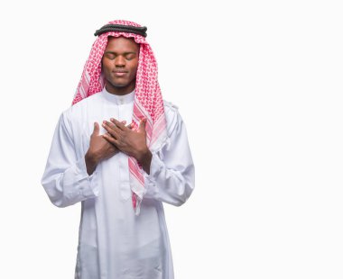 Geleneksel keffiyeh ile gülümseyen izole arka plan üzerinde giyen genç Arapça Afrika adam kapalı gözler ve yüzünde minnettar jest ile göğüs üzerinde eller. Sağlık kavramı.
