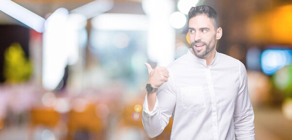 Young business man over isolated background smiling with happy face looking and pointing to the side with thumb up.