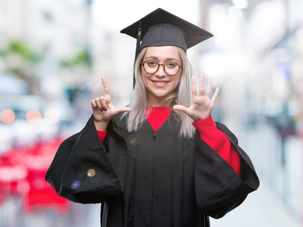 孤立した背景表示と指で上向きに大学院の制服を着て若いブロンドの女性数は自信を持って 幸せな笑みを浮かべている間 — ストック写真