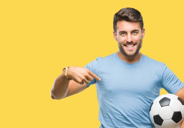 年轻英俊的男子拿着足球足球在孤立的背景和惊讶的脸指向自己的手指 — 图库照片