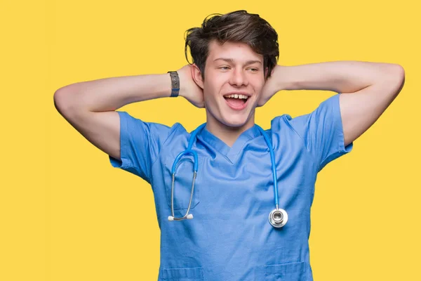 若い孤立の背景の上の身に着けている医療ユニフォームの医者リラックスして腕と頭と首 幸せな笑顔の後ろに手を伸ばす — ストック写真