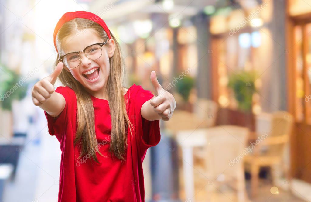 Young beautiful girl wearing glasses over isolated background approving doing positive gesture with hand, thumbs up smiling and happy for success. Looking at the camera, winner gesture.