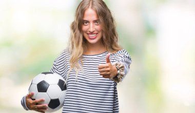 İzole arka plan üzerinde futbol futbol topu ok işareti, başparmak ile parmak, mükemmel işareti yapıyor kocaman bir gülümseme ile mutlu tutan genç güzel sarışın kadın