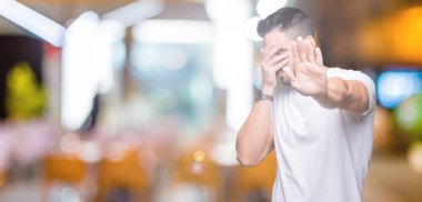 Genç adam gözleri elleriyle kapsayan izole arka plan üzerinde rahat beyaz t-shirt giyen ve stop jest ile acı ve korku ifadesi. Utandım ve negatif kavramı.