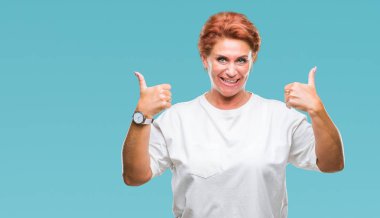 Atrractive üst düzey beyaz Kızıl saçlı kadın izole arka plan başarı işareti başparmak gülümseyen ve mutlu el ile olumlu hareketi yapıyor. Neşeli bir ifadeyle, kazanan jest kameraya bakıyor.