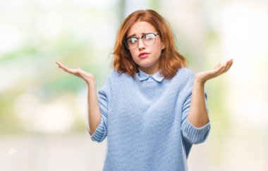 İzole arka plan kış kazak clueless ve şaşkın bir ifadeyle kollar ve eller kaldırdı giyen genç güzel kadın. Şüphe kavramı.