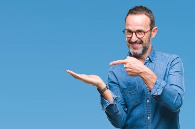 Orta yaş ağarmış komuta sizde hayrete ve el ile sunulması ve parmak ile işaret ederken kameraya gülümseyen izole arka plan üzerinde gözlük.