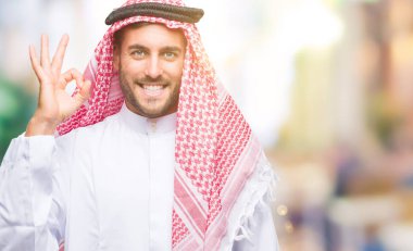 Keffiyeh izole arka plan el ve parmaklar ok işaretiyle yapıyor olumlu gülümseyen üzerinde giyen genç yakışıklı adam. Başarılı ifade.