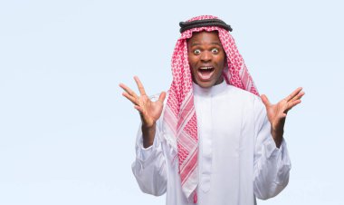 Geleneksel keffiyeh üzerinde giyen genç Arapça Afrika adam deli kutluyor arka plan izole ve başarı için kaldırdı kollarını açarak hayrete ve heyecanlı çığlık gözleri açık. Kazanan kavramı